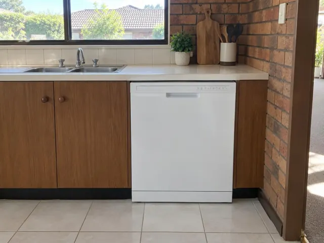 White dishwasher under a kitchen benchtop beside wood cabinets and a tiled splashback in Cardiff