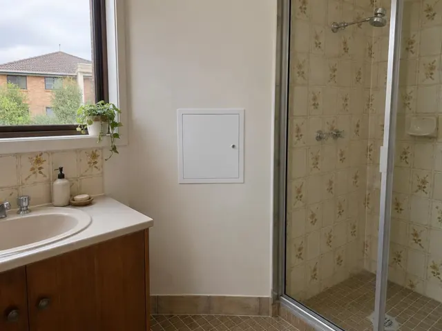 Bathroom wall with a small access panel beside a tiled shower and vanity in Cardiff