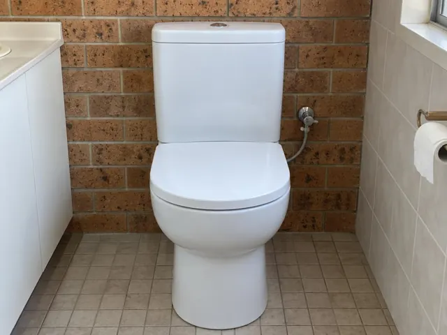 White toilet in a tiled bathroom with brick feature wall and window in Cardiff South